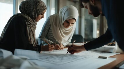 Women work, collaborating on architectural plans in modern workplace. Dressed stylish hijabs, professionalism, dedication. Teamwork, creative process in design. Architecture, culture.
