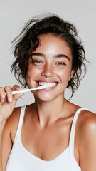 Jeune femme souriante se brossant les dents avec une brosse blanche