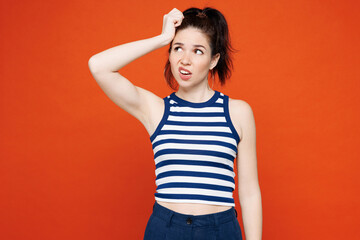 Young sad minded pensive woman wears blue striped tank top casual clothes put hand on head scratch temple look aside isolated on plain red orange color background studio portrait. Lifestyle concept.
