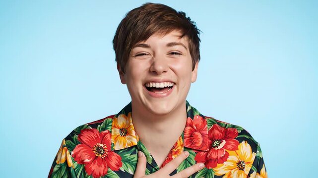 Happy young lady with a pixie cut hairdo sporting a vibrant flower patterned top, giggling genuinely in front of a soft blue backdrop in a studio setting