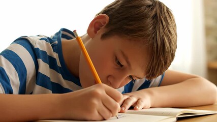 Diligent student sits at a desk, deeply focused on either writing or drawing in his notebook. The young boy shows great concentration as he engages in his schoolwork