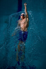 Male swimmer backstroke technique underwater with focus and control. Concept of swimming education, wellness, medical rehab, sports advertising, and motivational athletic performance.