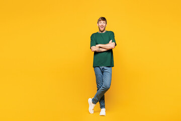 Full body young smiling happy man he wearing green t-shirt casual clothes hold hands crossed folded looking camera isolated on plain yellow orange color background studio portrait. Lifestyle concept.