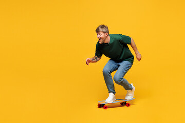 Full body side profile view happy cool young man he wear green t-shirt casual clothes riding skateboard pennyboard isolated on plain yellow orange wall background studio portrait. Lifestyle concept.