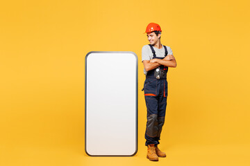 Full body young employee laborer handyman man he wear helmet overall stand near big huge blank...