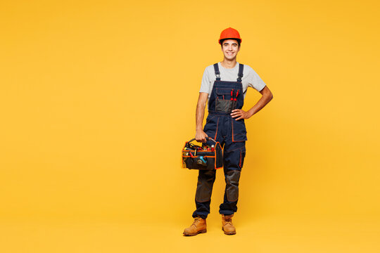 Fototapeta Full body young smiling happy employee laborer handyman man wear helmet overall hold bag with tools isolated on plain yellow background. Instruments for renovation apartment room. Repair home concept.