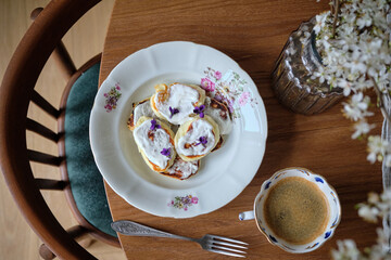 Pancakes with sour cream and wild viola on a beautiful porcelain plate. A white cherry branches in blossom period with white flowers and fresh green leaves in glass vase on a white table