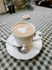 Warm coffee cup with heart foam art on checkered tablecloth in cozy cafe setting