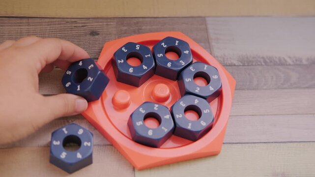 Hand placing numbered blue hexagonal puzzle pieces orange educational game board, developing logic and math skills, STEM toy, mental exercise, cognitive development, problem solving, matching numbers