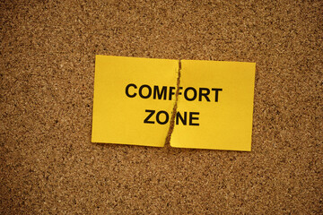 A ripped yellow paper note with the words Comfort Zone on it lying on a cork board. Close up.