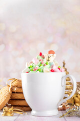 Festive tasty Christmas hot chocolate with green and red colored whipped cream, with marshmallow and sugar holiday decorations on top, on festive holiday decorated  background