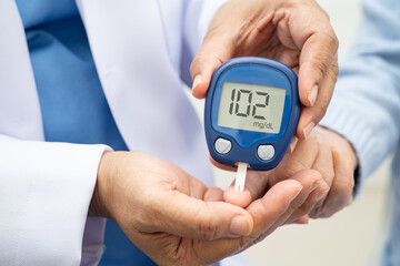 Asian doctor using digital glucose meter for check sample blood sugar level to treatment diabetes.