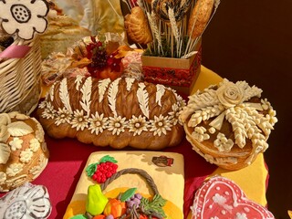 An assortment of beautifully decorated breads and pastries on display. The centerpiece is a braided loaf adorned with floral patterns, surrounded by various artisanal baked goods.