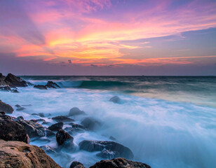 Naklejka premium Serene Sunset Over Gentle Waves and Rocky Shoreline at Dusk