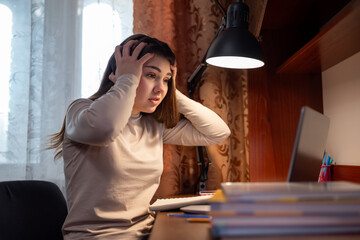 A student in despair from the volume of her homework. A girl holds her head in her hands as she looks at a laptop, shocked by the amount of homework and the difficulty of the exercises