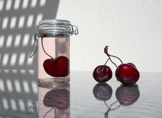 Still life with sweet cherry berries and a small fruit jar of compote on a glass-topped table. 