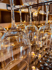 A close-up view of upside-down wine glasses hanging on a rack, surrounded by warm glowing string lights.