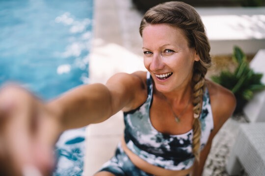 Close-up portrait of smiling blonde woman taking selfie by pool, joyful and confident, radiating wellness and happiness, captured in bright outdoor resort environment
