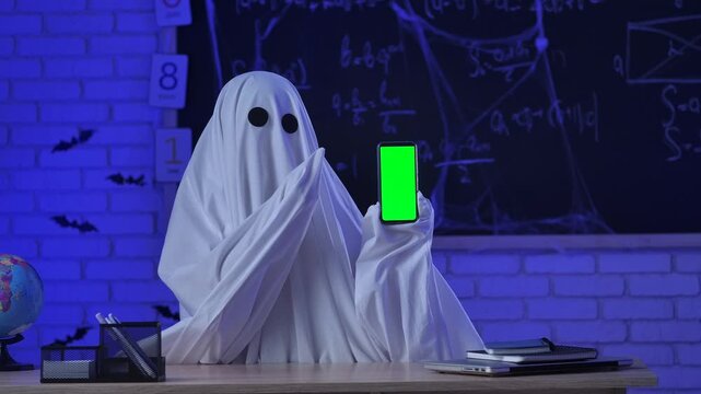 A person in a white ghost sheet shows a smartphone with a green screen