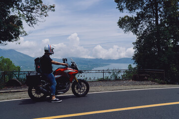 Motorcyclist parked by guardrail with smartphone and GPS equipment, enjoying elevated view while relying on tech for orientation in scenic but unfamiliar environment.