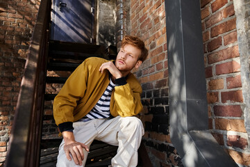 Handsome redhead man in stylish autumn outfit poses in city alleyway
