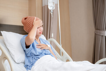 Asian young woman in bed suffering from cancer. Young patient headscarf recovery in hospital on bed.