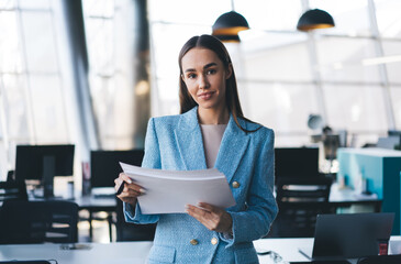 Freelancer stands with printed documents, poised and attentive, bridging digital structure with...