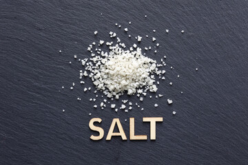 Dried coarse salt on black slate background with wooden word Salt