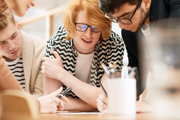 Team work. Group of enthusiastic young workers standing bent over table in conference room and creating plan for further company development, close-up view