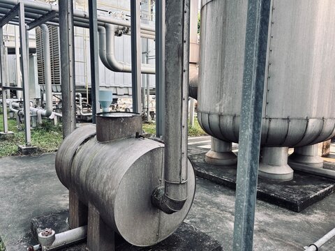 A collection of industrial water storage tanks, cooling units, and pressure vessels with visible aging and piping, symbolizing outdated infrastructure, water management, and heavy factory equipment 
