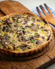 French quiche with wild mushrooms, egg, and beef on a wooden table.