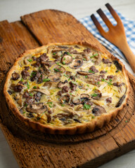French quiche with wild mushrooms, egg, and beef on a wooden table.