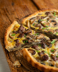 French quiche with wild mushrooms, egg, and beef on a wooden table.