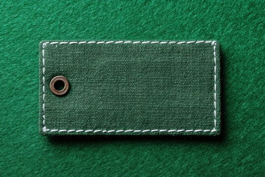 Blank Green Rectangular Label with Stitched Border Edges for Text Space on Emerald. Pristine fabric clothing label with tightly woven textile texture. Leather mockup. Clear adherent tag. Empty oblong
