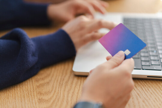 A person holds a credit card, preparing for an online transaction. Their other hand types on a laptop keyboard, demonstrating digital payment or banking.