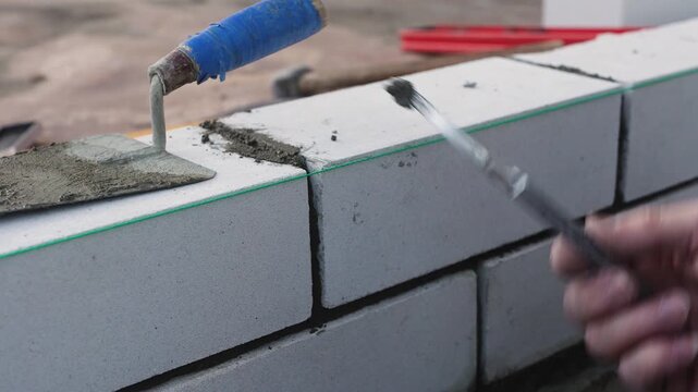Masonry worker building a wall from aerated concrete blocks with cement mortar