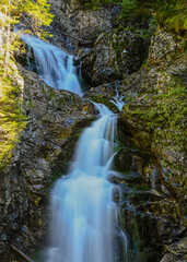 Fototapeta premium Kmeťov waterfall flowing over moss-covered rocks in a green forest with a long exposure effect