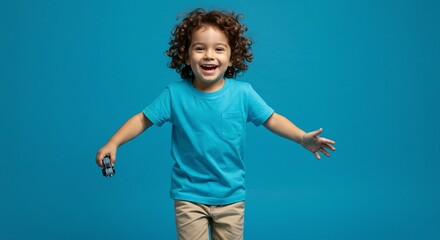 Joyful young boy with curly hair smiles against a blue backdrop, holding a toy car with arms outstretched in a welcoming gesture.
