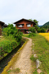 Fototapeta premium 白川郷の田んぼと澄んだ用水路に面した伝統的な木造家屋 