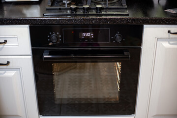 A modern built-in oven with a digital clock is integrated into a kitchen with white cabinets and a...