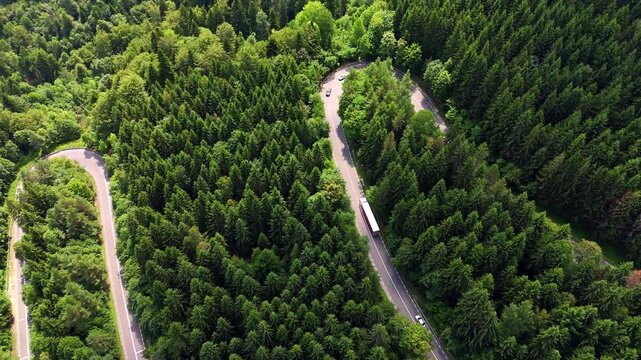 Wavy highway in the green pine tree woods covering the mountains. Travelling by the Carpathian Mountains in Romania. Aerial view.