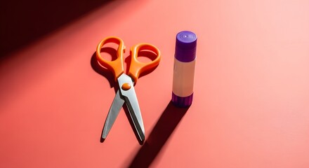Scissors and glue stick on a red surface, crafting tools.