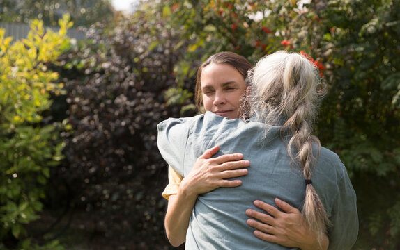 an elderly woman hugs her adult daughter near the house in the garden. Deep conversation. emotional intimacy. support in two age generations
