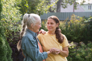 Fototapeta premium an elderly woman hugs her adult daughter near the house in the garden. Deep conversation. emotional intimacy. support in two age generations