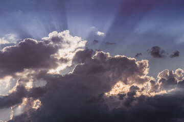 Dark cumulus clouds filling the sky, sunbeams piercing through silver linings, creating a beautiful moody atmosphere