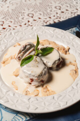 Close-up view of round pieces of meat with white sauce and a stylized leaf on a plate.