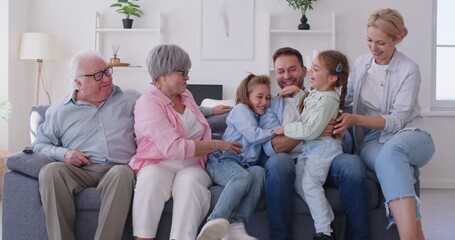 Happy big family having fun tickling with cute little children sitting on sofa at home. Parents, grandparents and kids spending time together. Family leisure concept. 4k video. Slow motion video. - Powered by Adobe