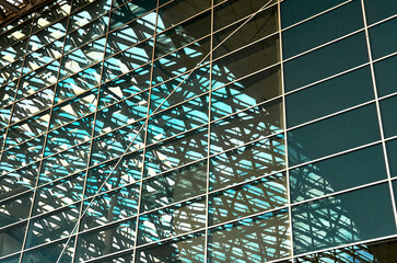 A modern building made of glass and metal, the glass reflects the metal structures of the neighboring building, forming a curvy architectural abstraction.