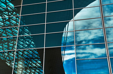 The wall of the building, made of glass and metal frames, the sky and other parts of the building are reflected in the windows, a beautiful architectural abstraction