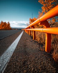 Asphalt Road Perspective with Orange Guardrail and Autumnal Trees Under a Bright Blue Sky.